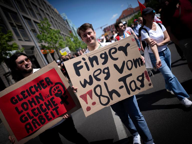 Demonstranten halten Plakate hoch: "Finger weg vom 8-Stunden-Tag" und "Gleicehr Lohn für gleiche Arbeit". Demonstranten halten Plakate hoch: "Finger weg vom 8-Stunden-Tag" und "Gleicehr Lohn für gleiche Arbeit".