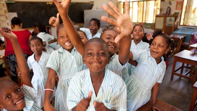Schulkinder auf den Sychellen in Afrika. Die Schülerinnen und Schüler stehen zusammen und winken und lachen in die Kamera. 