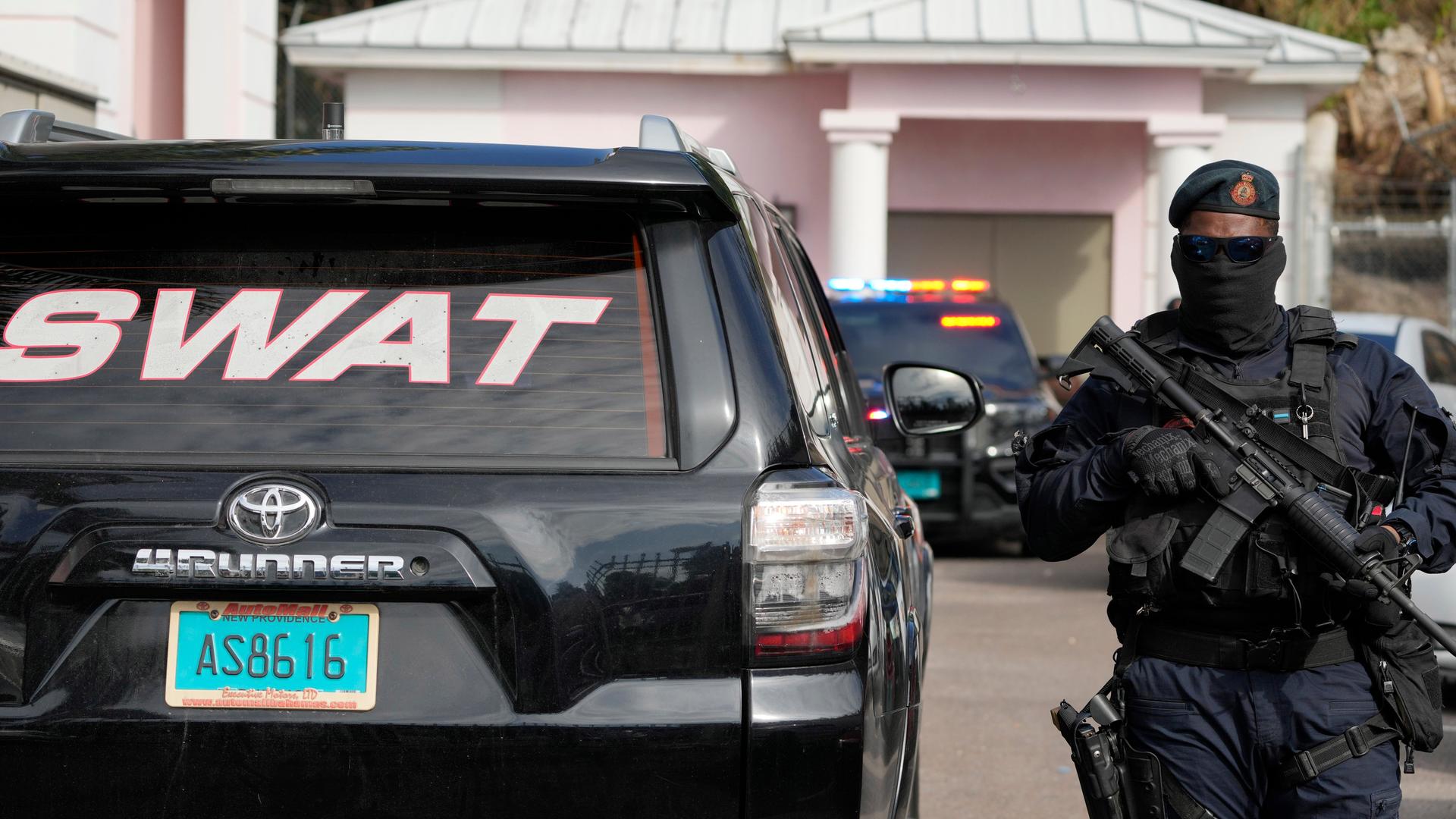 Ein Sicherheitsbeamter steht mit einer Maske, Sonnenbrille und einem Gewehr im Anschlag vor dem Gerichtsgebäude in Nassau. Neben ihm steht ein Polizeiwagen mit der Aufschrift "Swat". Ein Sicherheitsbeamter steht mit einer Maske, Sonnenbrille und einem Gewehr im Anschlag vor dem Gerichtsgebäude in Nassau. Neben ihm steht ein Polizeiwagen mit der Aufschrift "Swat".