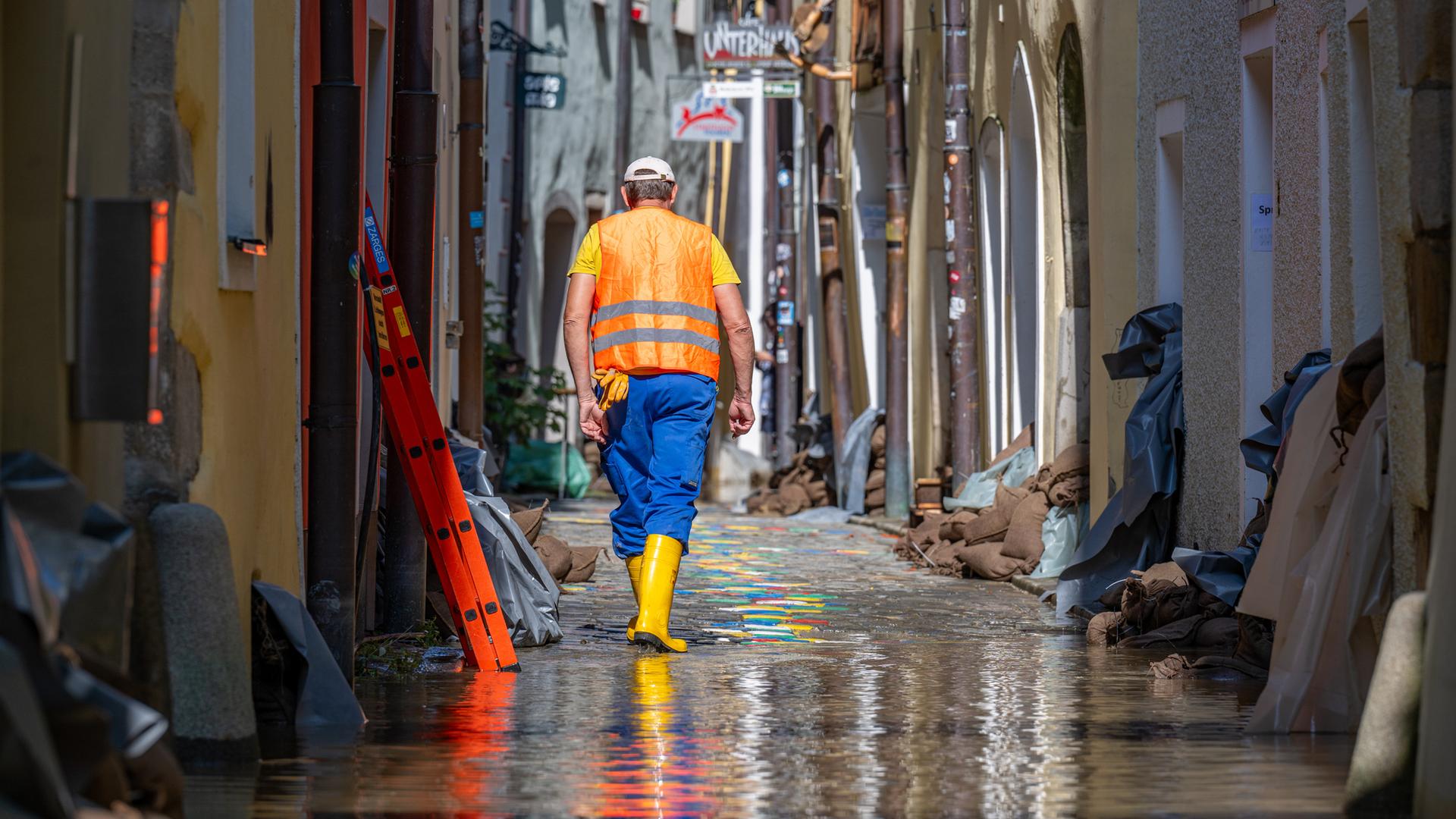 Ein Helfer geht, nachdem das Hochwasser der Donau etwas zurückgegangen ist, durch eine Gasse mit Sandsäcken vor den Häusern.