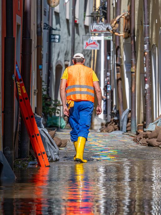 Ein Helfer geht, nachdem das Hochwasser der Donau etwas zurückgegangen ist, durch eine Gasse mit Sandsäcken vor den Häusern.