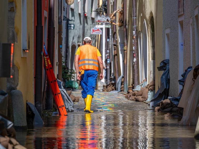 Ein Helfer geht, nachdem das Hochwasser der Donau etwas zurückgegangen ist, durch eine Gasse mit Sandsäcken vor den Häusern.