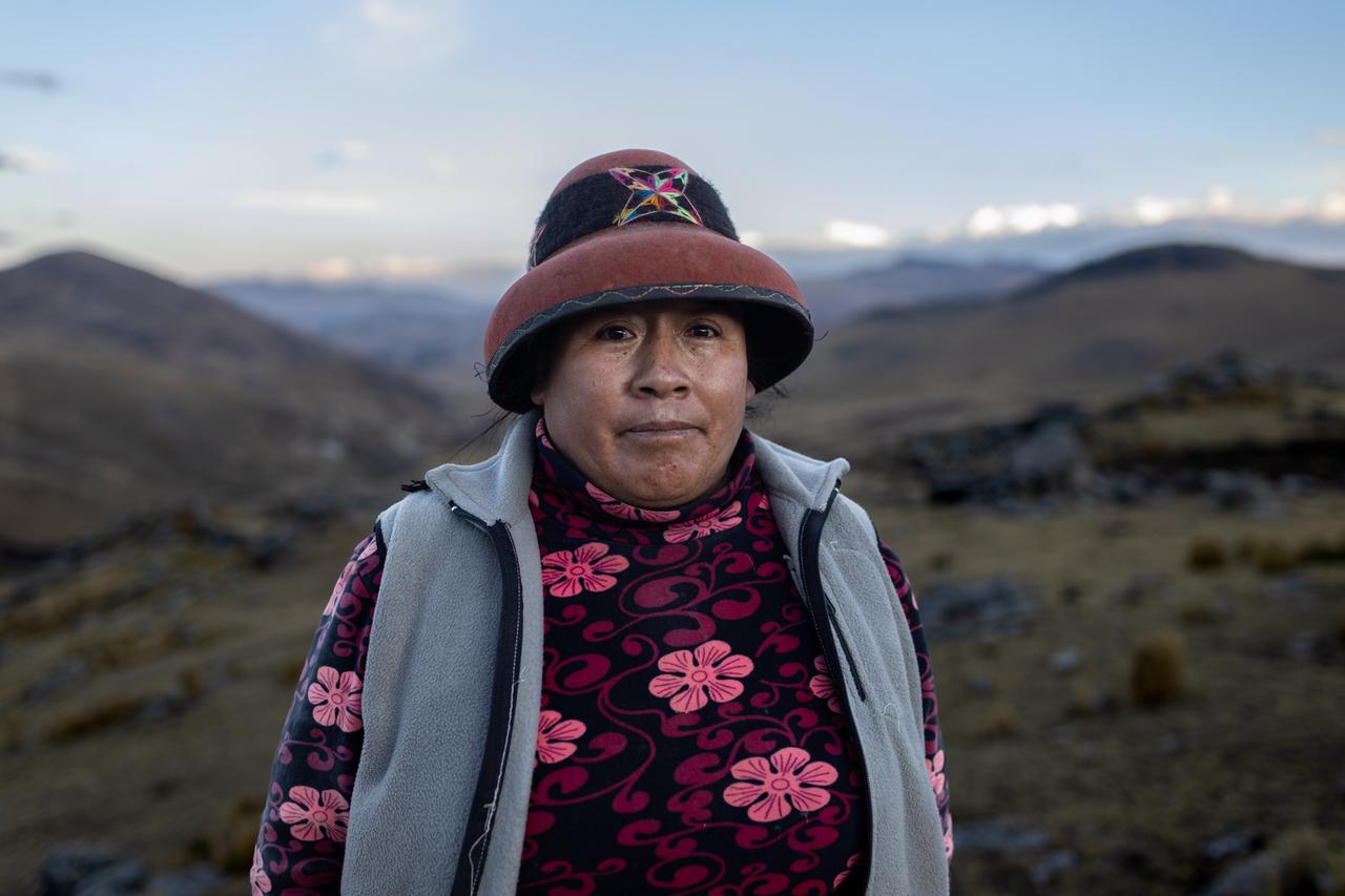Marcusa Huamani steht im Andenhochland von Peru und trägt traditionelle Kleidung ihrer indigenen Gemeinde mit Blumenmuster und einen Hut.