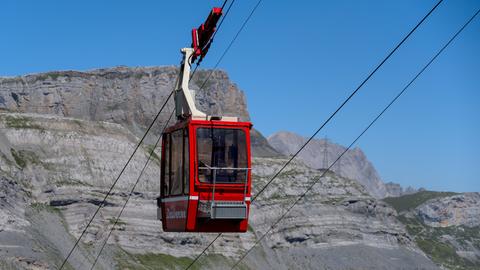 Eine rote Gondel einer Schweizer Seilbahn auf ihrer Fahrt in hohe, kahle Berge.