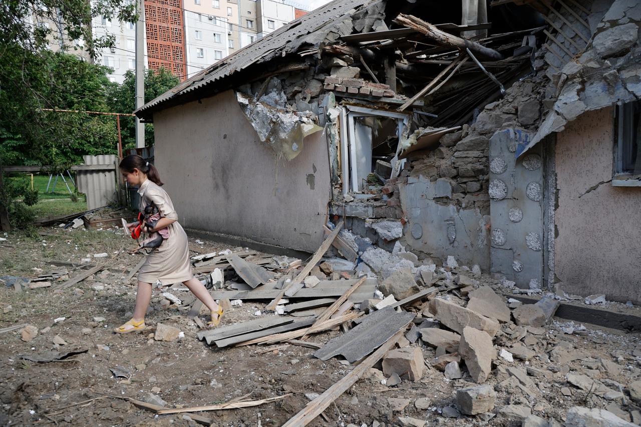 Ein Mädchen in Donezk trägt einen Hund an einem zerstörten Haus vorbei. 