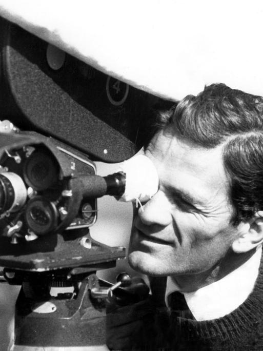 Pier Paolo Pasolini an einem Filmset im Jahr 1962. Er schaut durch eine Kamera.