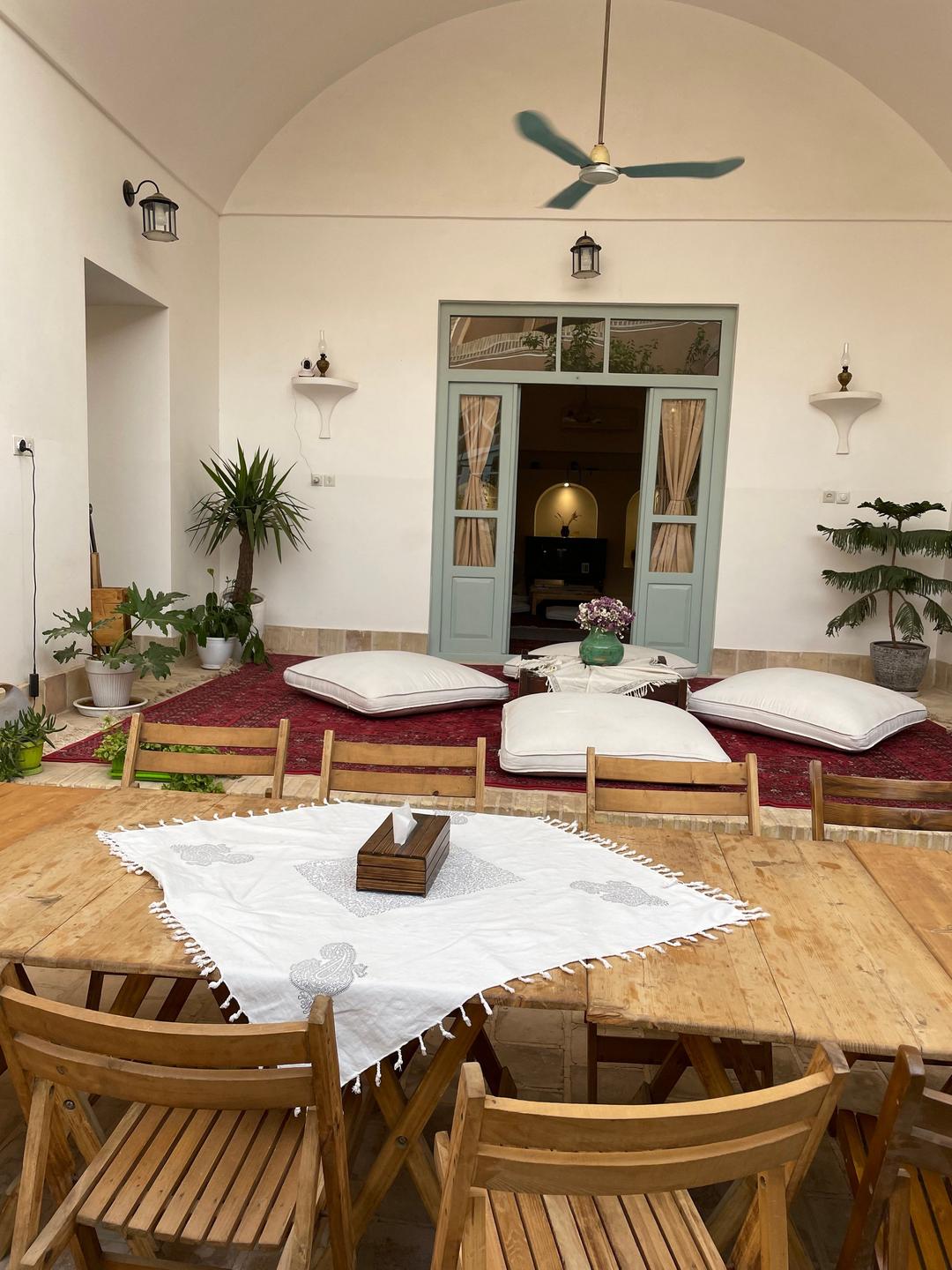 Innenhof des Hotels "Wadi-Haus" mit Blick in den Gemeinschaftsraum mit Holztisch, Stühlen und großen weißen Kissen am Boden.