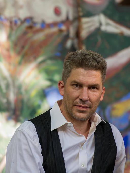 Autor Murmel Clausen sitzt im Künstlergarten Weimar vor einer bunt bemalten Wand.
