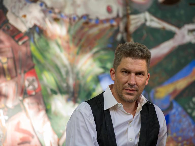 Autor Murmel Clausen sitzt im Künstlergarten Weimar vor einer bunt bemalten Wand.