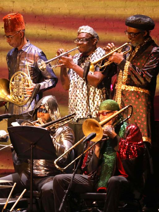 Die Bläser-Sektion des Sun Ra Arkestra spielt auf einer Bühne. Die Musiker sind in farbenfrohe Gewänder gekleidet. 