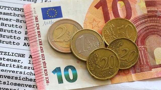 Auf einer Gehalts-Abrechnung liegen ein 10-Euro-Schein und mehrere Münzen.