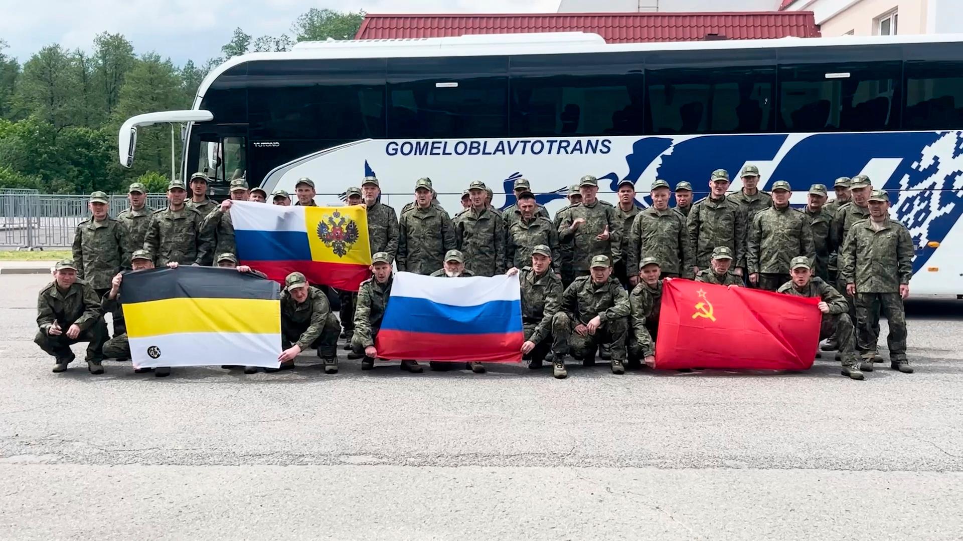 Das Foto, freigegeben vom Verteidigungsministerium in Moskau, zeigt russische Soldaten nach ihrer Übergabe aus ukrainischer Gefangenschaft. Sie posieren vor einem Bus und halten Flaggen in die Höhe. 
