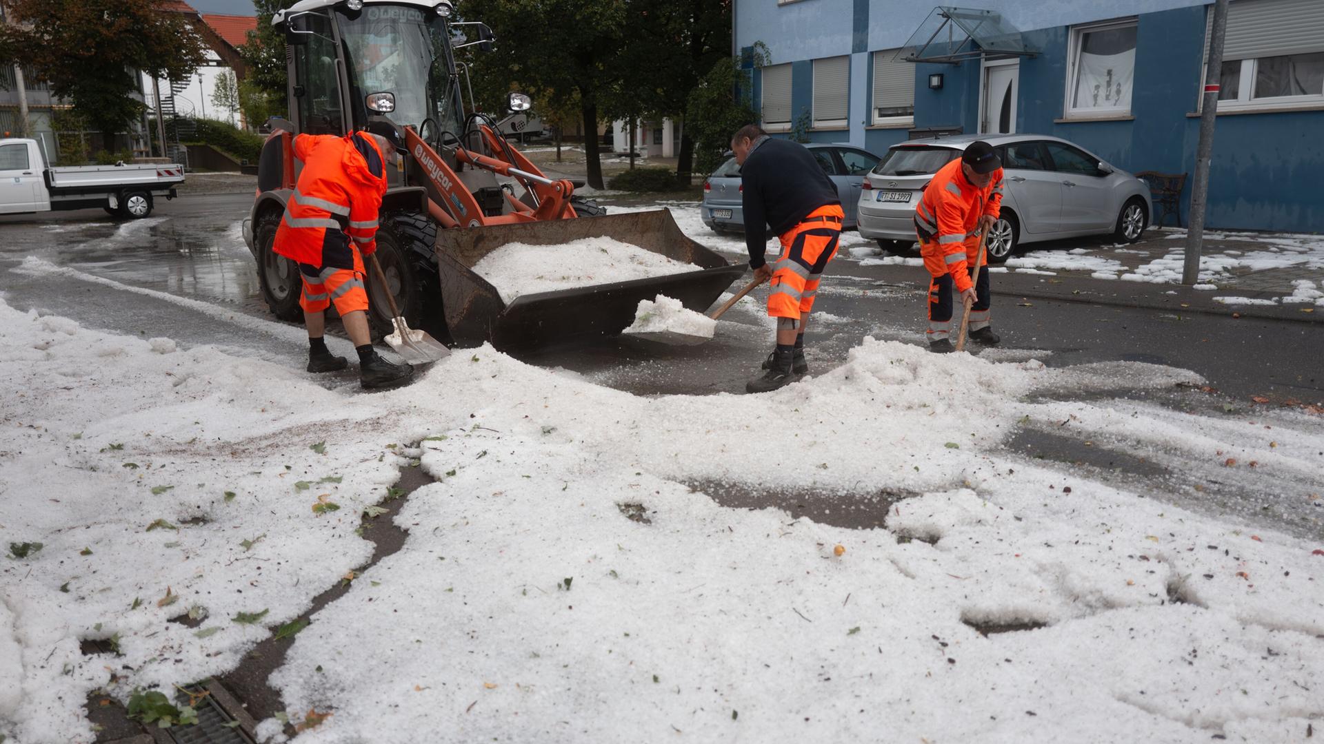 Arbeiter räumen große Mengen Hagelkörner von der Straße.