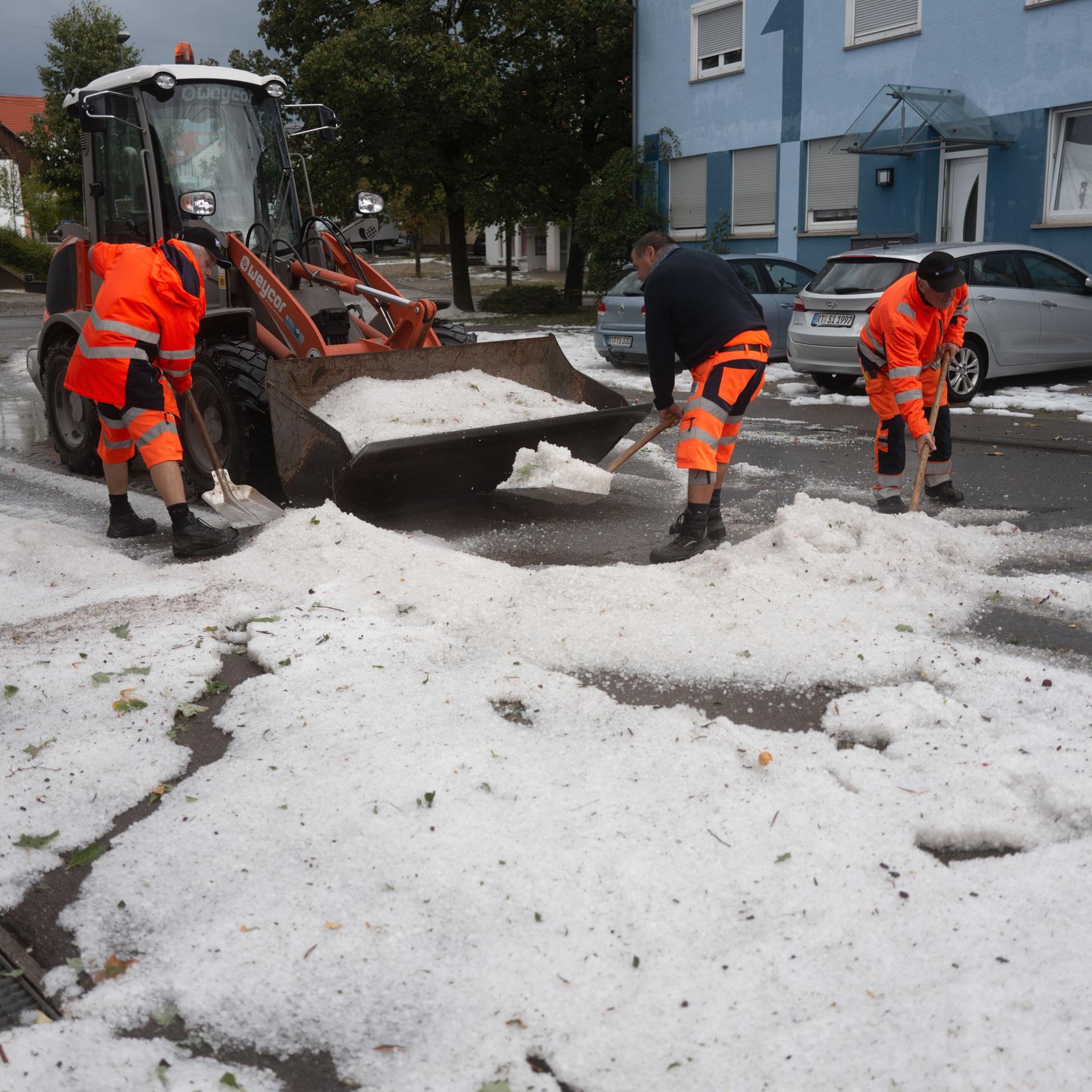 Arbeiter räumen große Mengen Hagelkörner von der Straße.