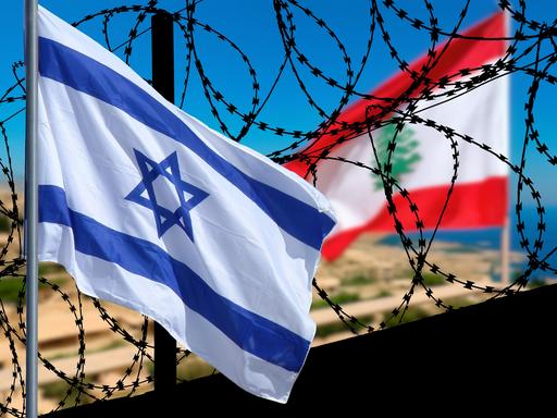 Die israelische und die libanesische Flagge wehen an einer Grenzanlage mit Stacheldraht.