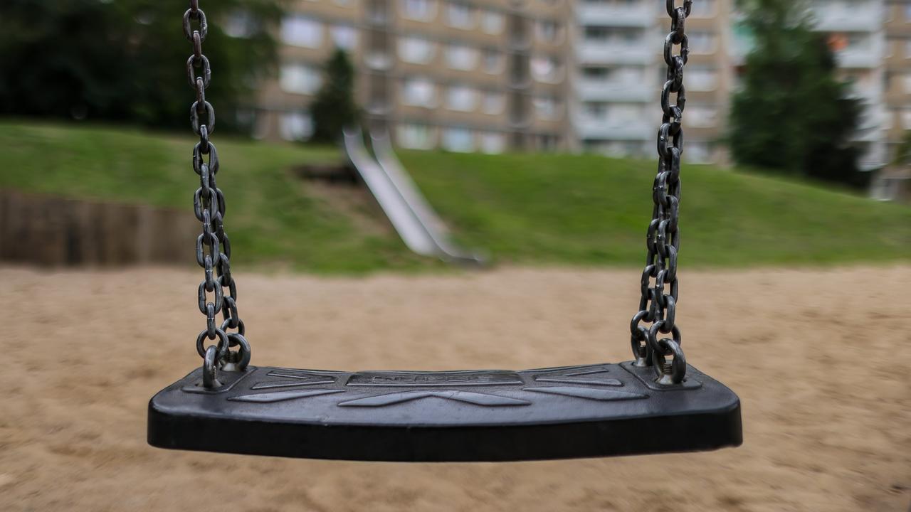 Ein leerer Spielplatz im Leipziger Stadtteil Grünau: Eine Schaukel ist im Vorderung, im Hintergrund die Plattenbau-Häuser Grünaus.