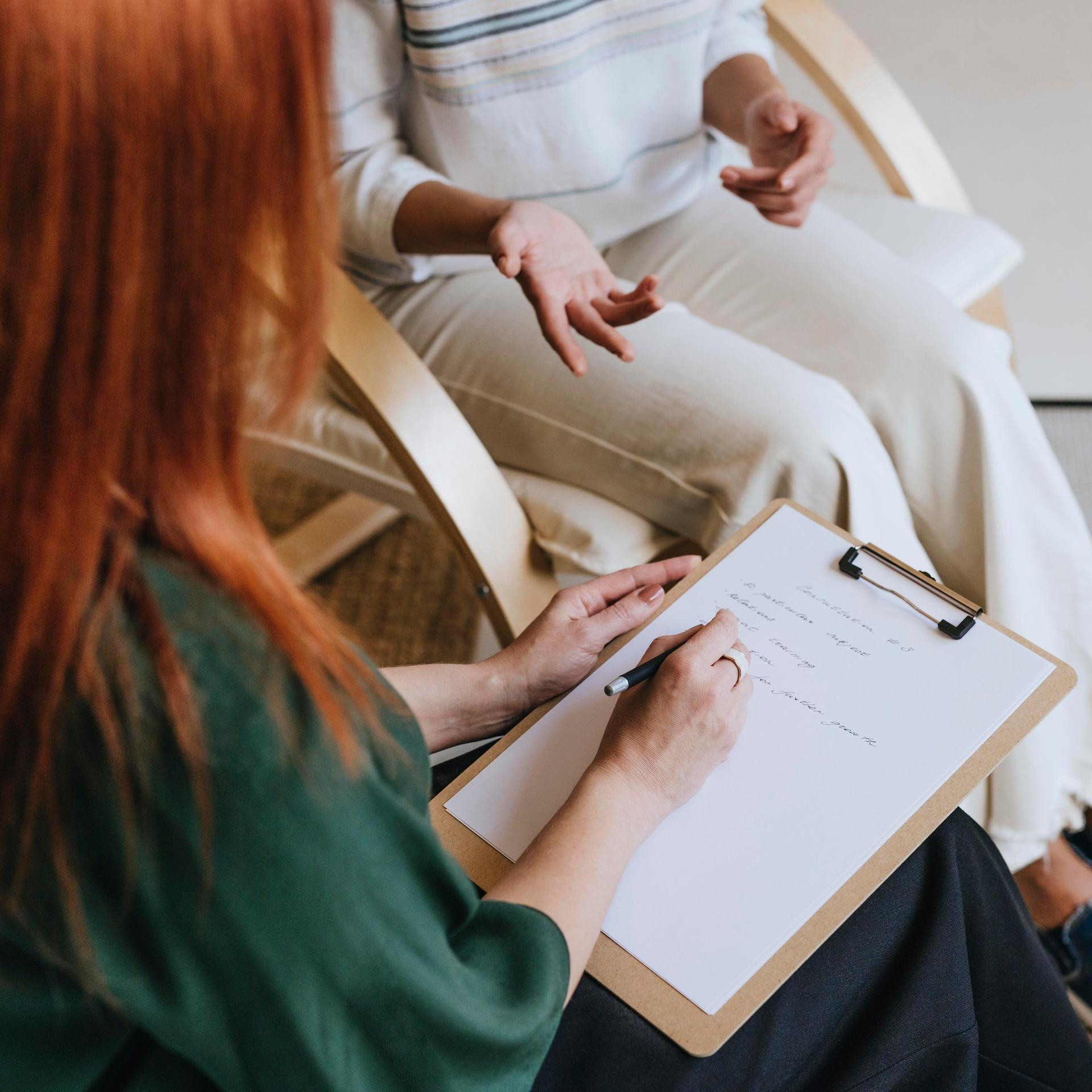 Zwei Personen sitzen zusammen und unterhalten sich, während eine der beiden sich Notizen macht