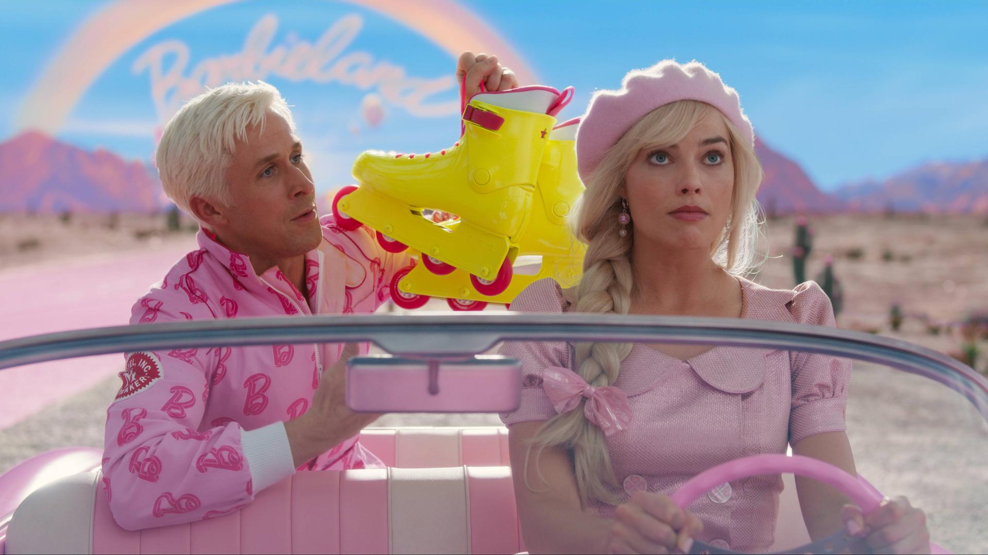 Das Foto zeigt ein Bild aus dem Barbie-Film. Links ist Ken und rechts ist Barbie am Steuer von dem Auto. 