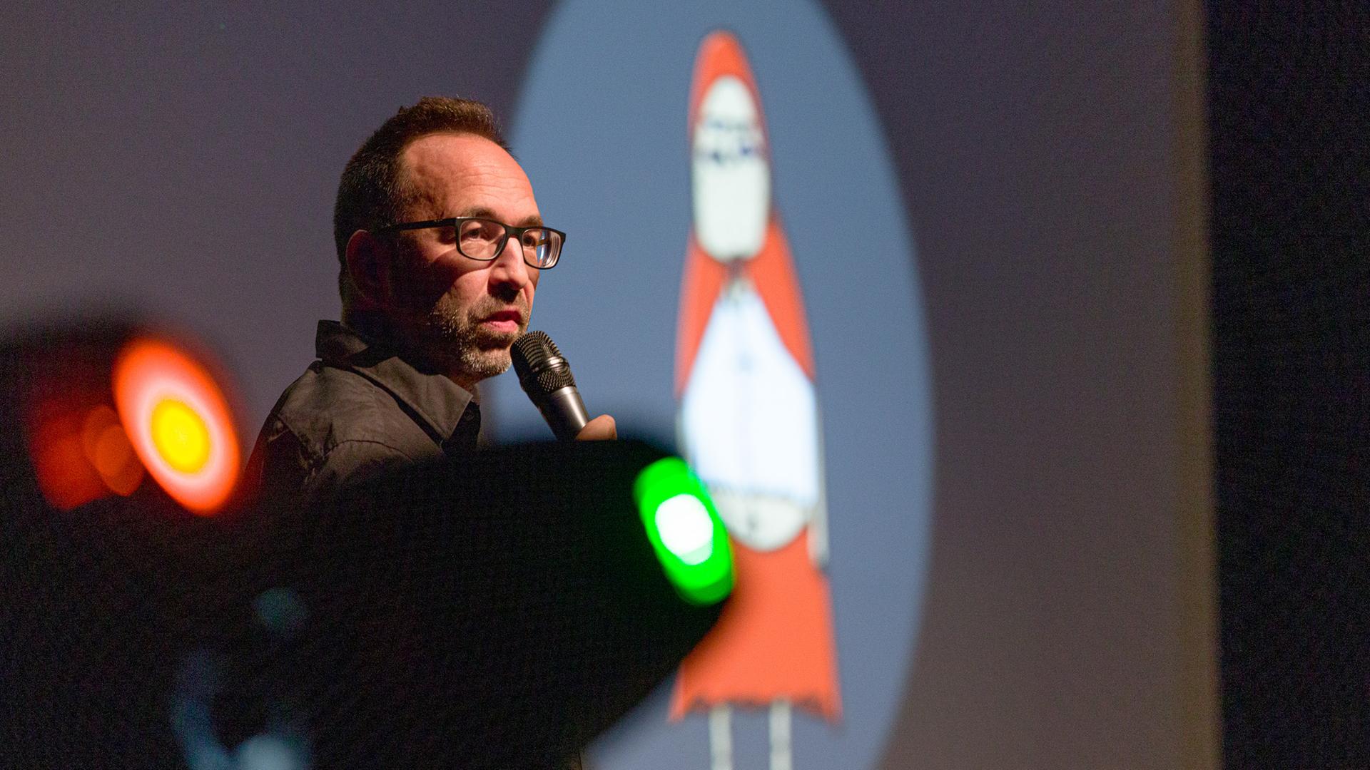 Piero Masztalerz steht beim ComedyArts-Festival 2022 in Moers mit einem Mikrofon auf der Bühne. Im Hintergrund ist ein Weihnachtsmann-Cartoon von ihm zu sehen.