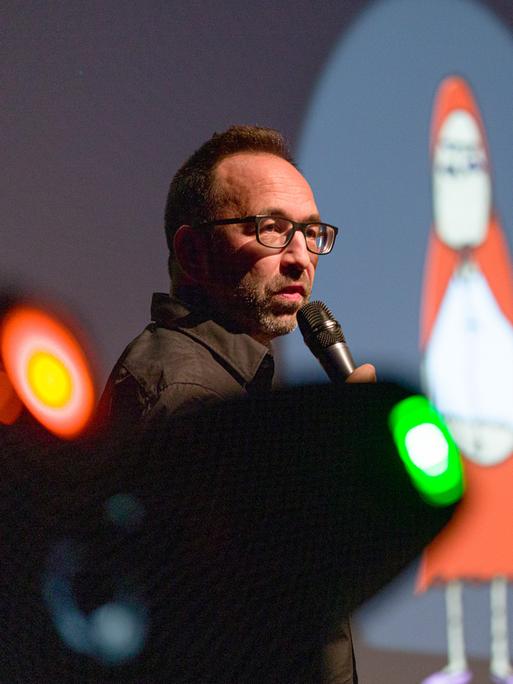 Piero Masztalerz steht beim ComedyArts-Festival 2022 in Moers mit einem Mikrofon auf der Bühne. Im Hintergrund ist ein Weihnachtsmann-Cartoon von ihm zu sehen.