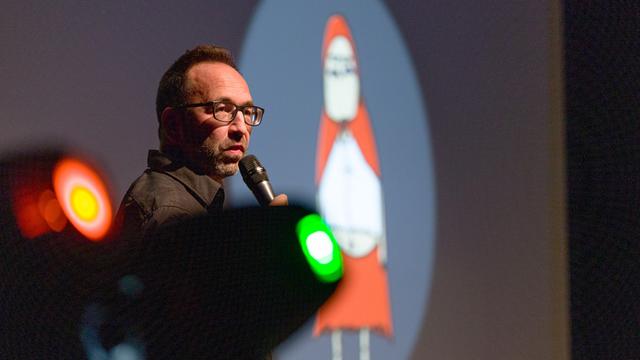 Piero Masztalerz steht beim ComedyArts-Festival 2022 in Moers mit einem Mikrofon auf der Bühne. Im Hintergrund ist ein Weihnachtsmann-Cartoon von ihm zu sehen.