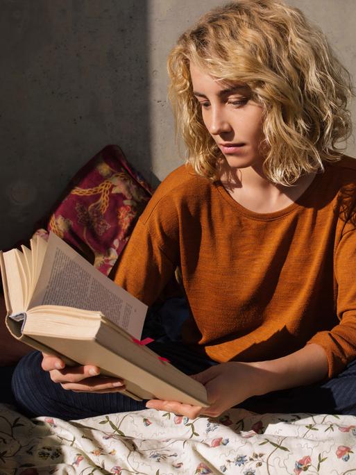 Eine Frau sitzt auf einem Sofa und liest ein umfangreiches Buch.