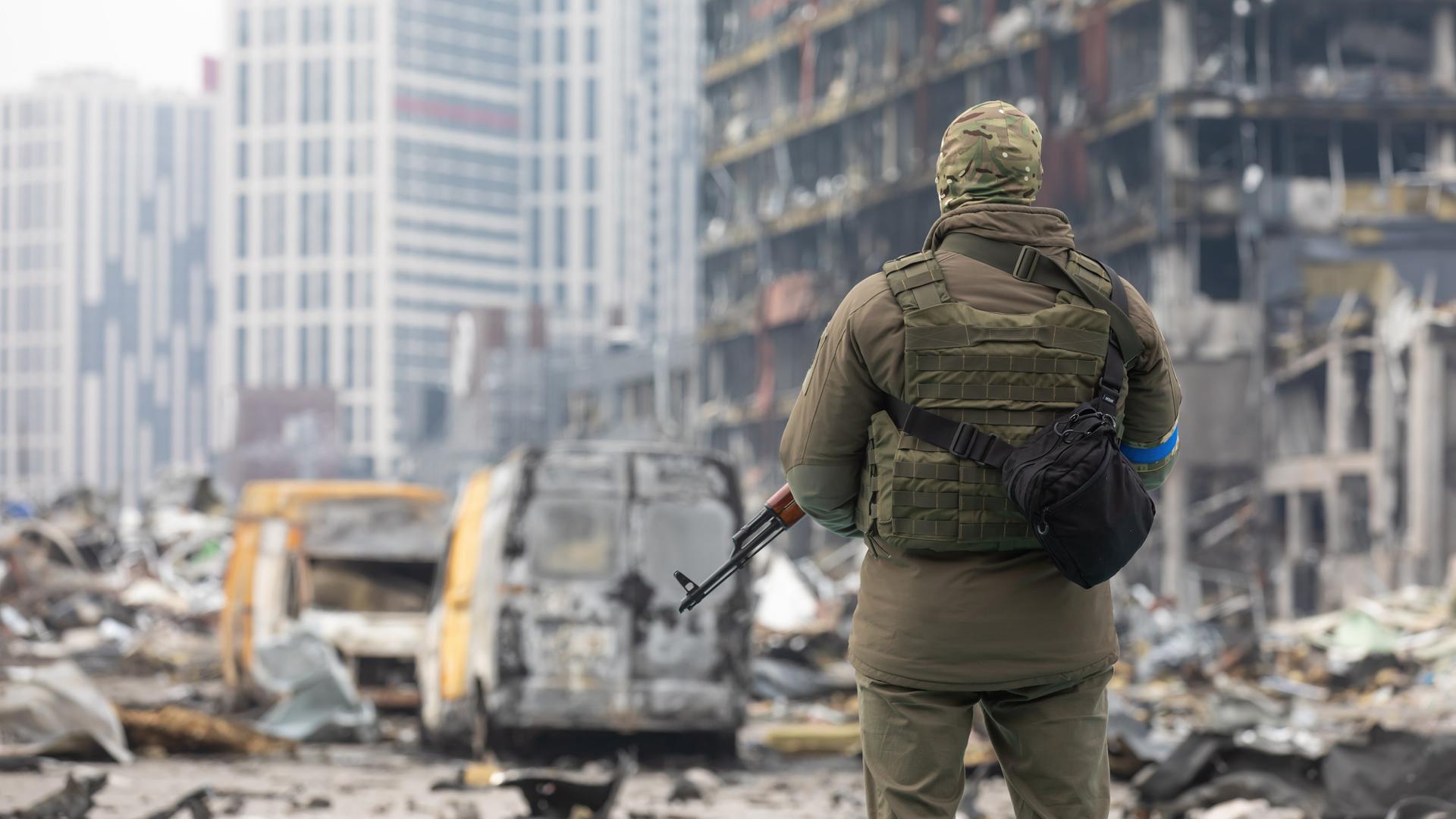 Ein ukrainischer Soldat steht mit einem Waffe in der Hand vor einem zerstörten Gebäude in Kiew. 