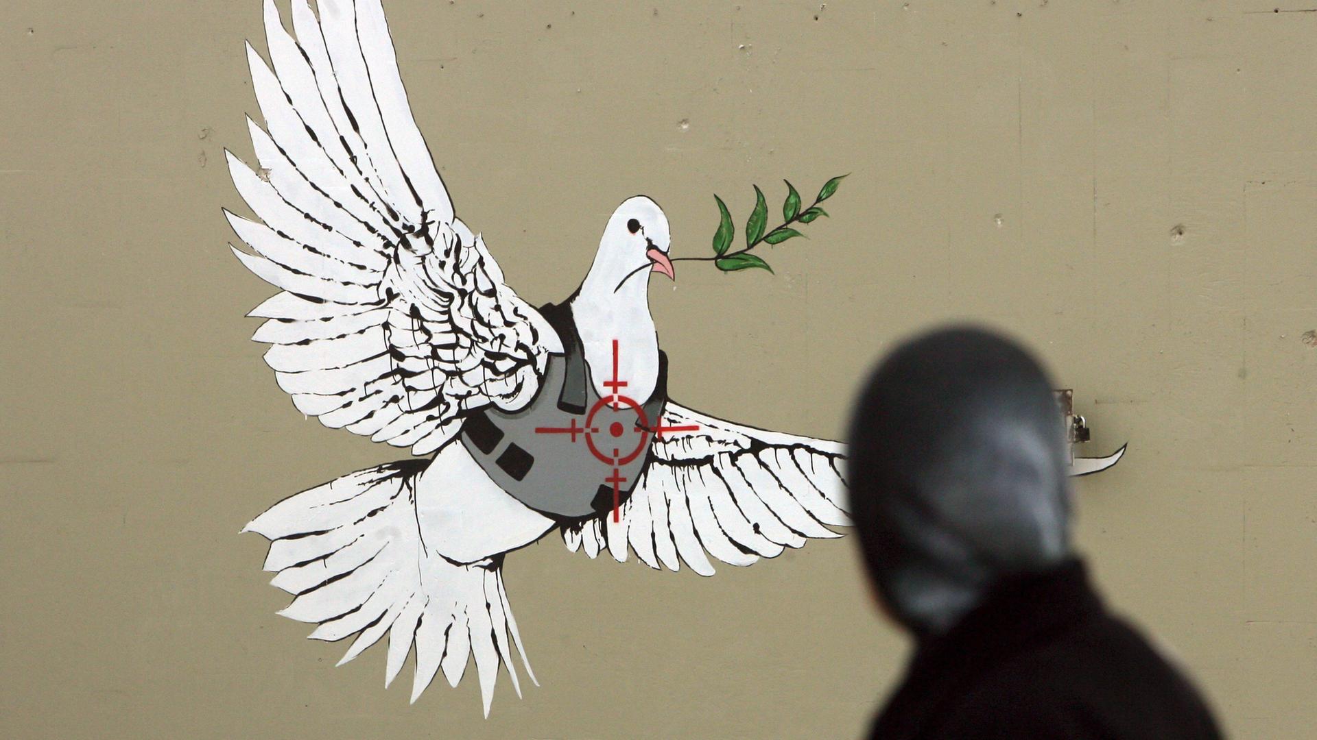 Grafitti des Streetart Künstlers Banksy in Bethlehem. Eine Friedenstaube mit Schussicherer Weste und dem Fadekreuz eines Scharfschützen auf dem Herzen.