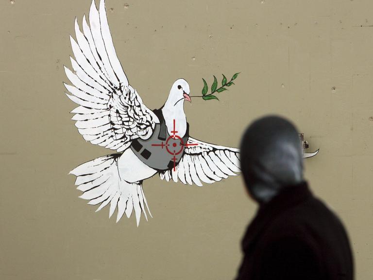 Grafitti des Streetart Künstlers Banksy in Bethlehem. Eine Friedenstaube mit Schussicherer Weste und dem Fadekreuz eines Scharfschützen auf dem Herzen.