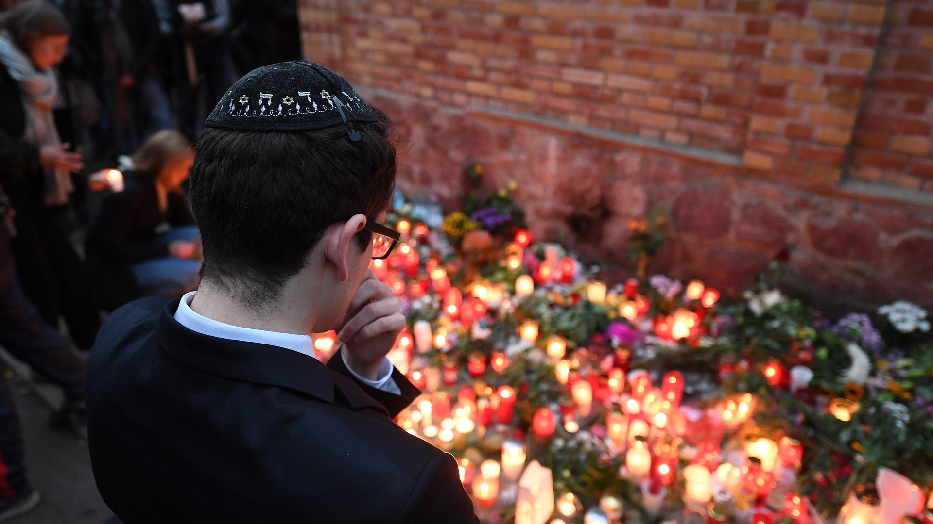 Ein junger Mann mit Kippa steht vor Gedenkkerzen an der Mauer zur Synagoge in Halle/Saale. 