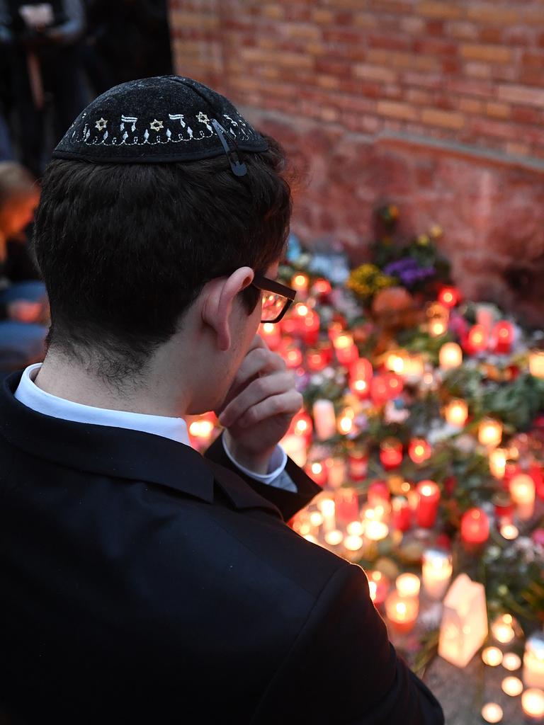 Ein junger Mann mit Kippa steht vor Gedenkkerzen an der Mauer zur Synagoge in Halle/Saale. 