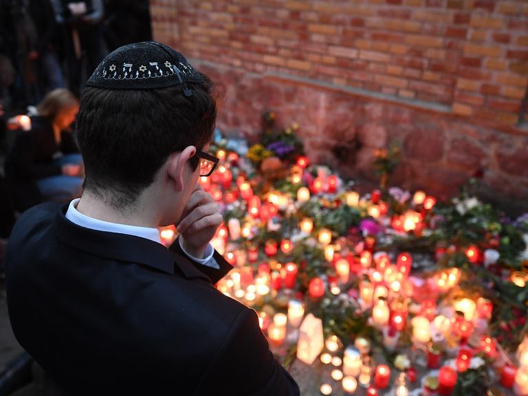 Ein junger Mann mit Kippa steht vor Gedenkkerzen an der Mauer zur Synagoge in Halle/Saale. 