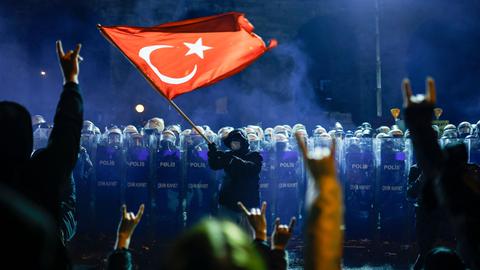 Ein Demonstrant reckt eine türkische Flagge in die Höhe. Dahinter stehen eng aufgereiht Polizisten in Kampfmonitur.