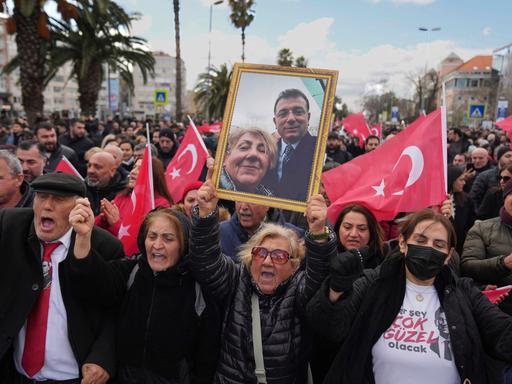 Ein Demonstrantin reckt ein gerahmtes Foto von ihr und Imamoglu in die Höhe. Um sie herum tausende weiterer Demonstranten u.a. mit türkischen Flaggen.