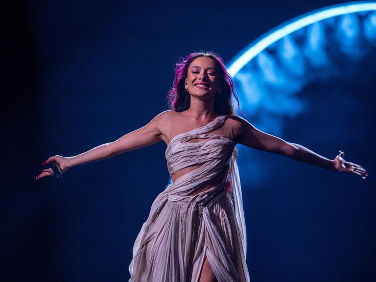 Das Bild zeigt die israelische Sängerin Eden Golan am 09.05.2024 beim zweiten Halbfinale des Eurovision Song Contest im schwedischen Malmö. Sie steht vor einer blau leuchtenden Bühnen-Dekoration und breitet die Arme aus.