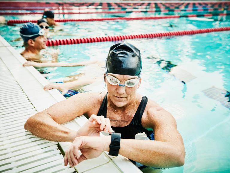 Eine Schwimmerin, die während ihres morgendlichen Trainings im Hallenbad auf ihre Fitnessuhr schaut