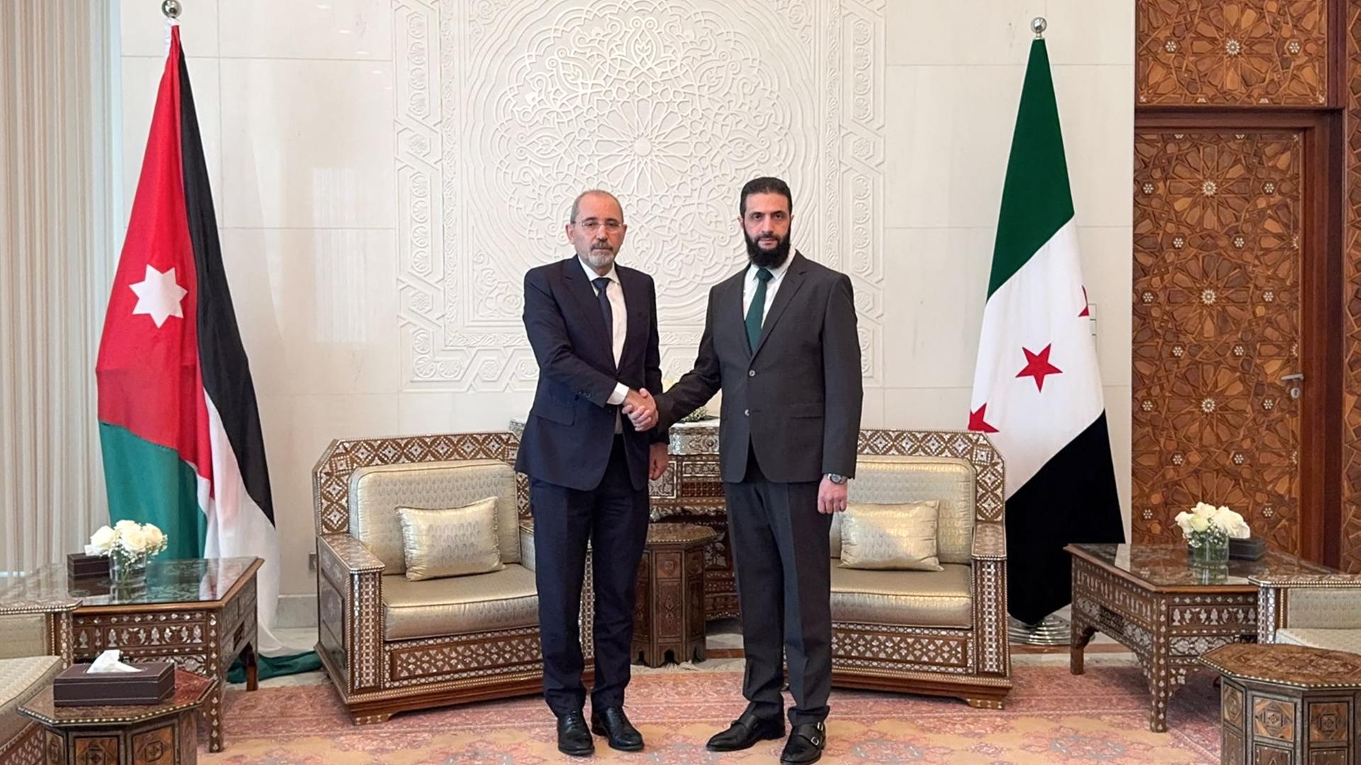 Jordaniens Außenminister Safadi (l) und der syrische Rebellenführer al-Sharaa reichen sich die Hand. Im Hintergrund die Flaggen der beiden Länder. Jordaniens Außenminister Safadi (l) und der syrische Rebellenführer al-Sharaa reichen sich die Hand. Im Hintergrund die Flaggen der beiden Länder.
