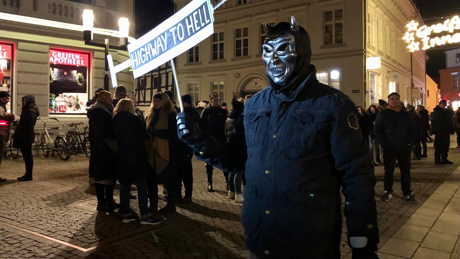 Ein Mann mit Teufelsmaske trägt bei einer Demonstration ein Schild mit der Aufschrift "Highway To Hell".