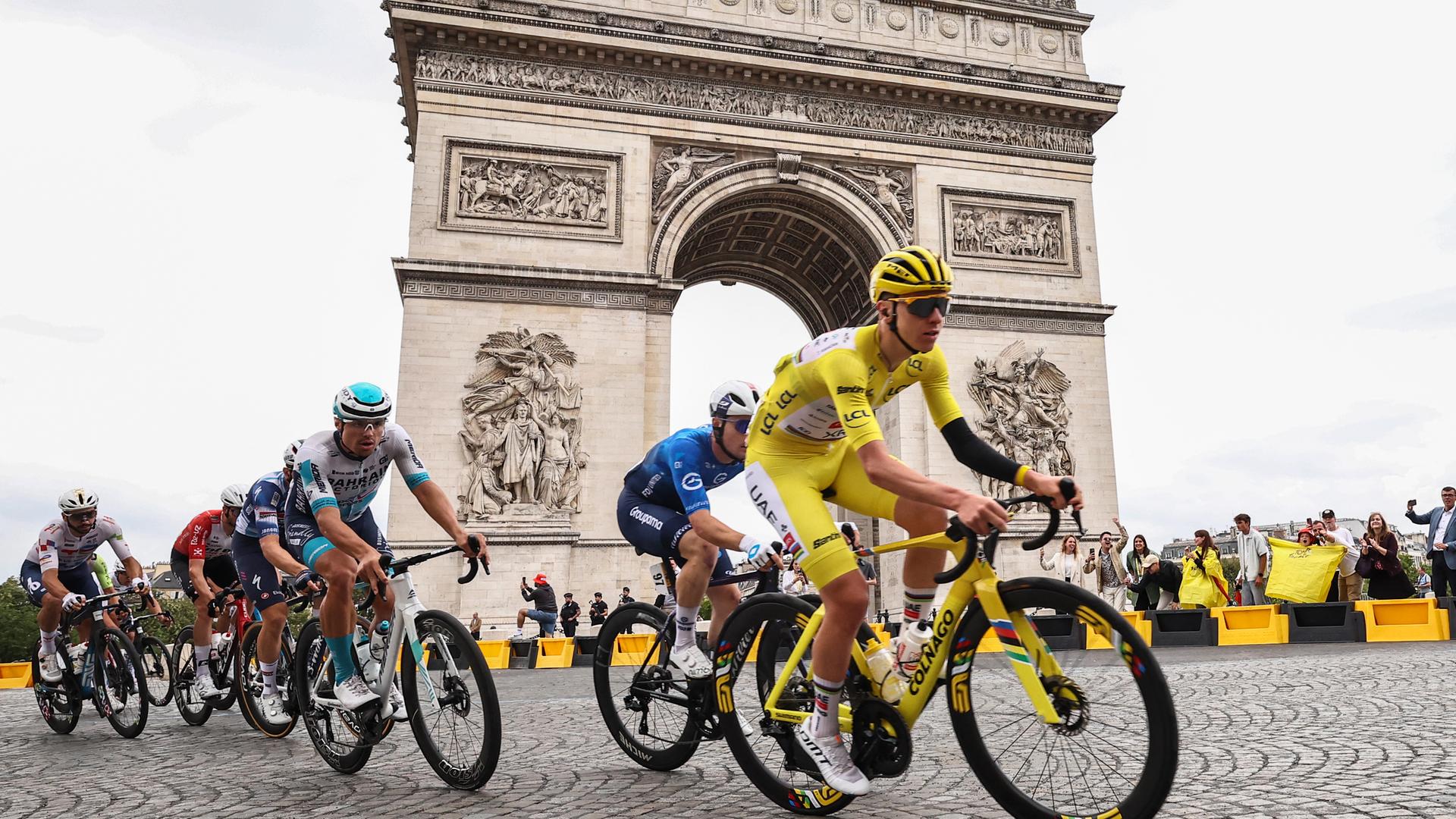 Tadej Pogacar fährt vor anderen Rennradfahrern auf den Pariser Champs-Élysées, hinter ihm ist der Arc de Triomphe im Bild.