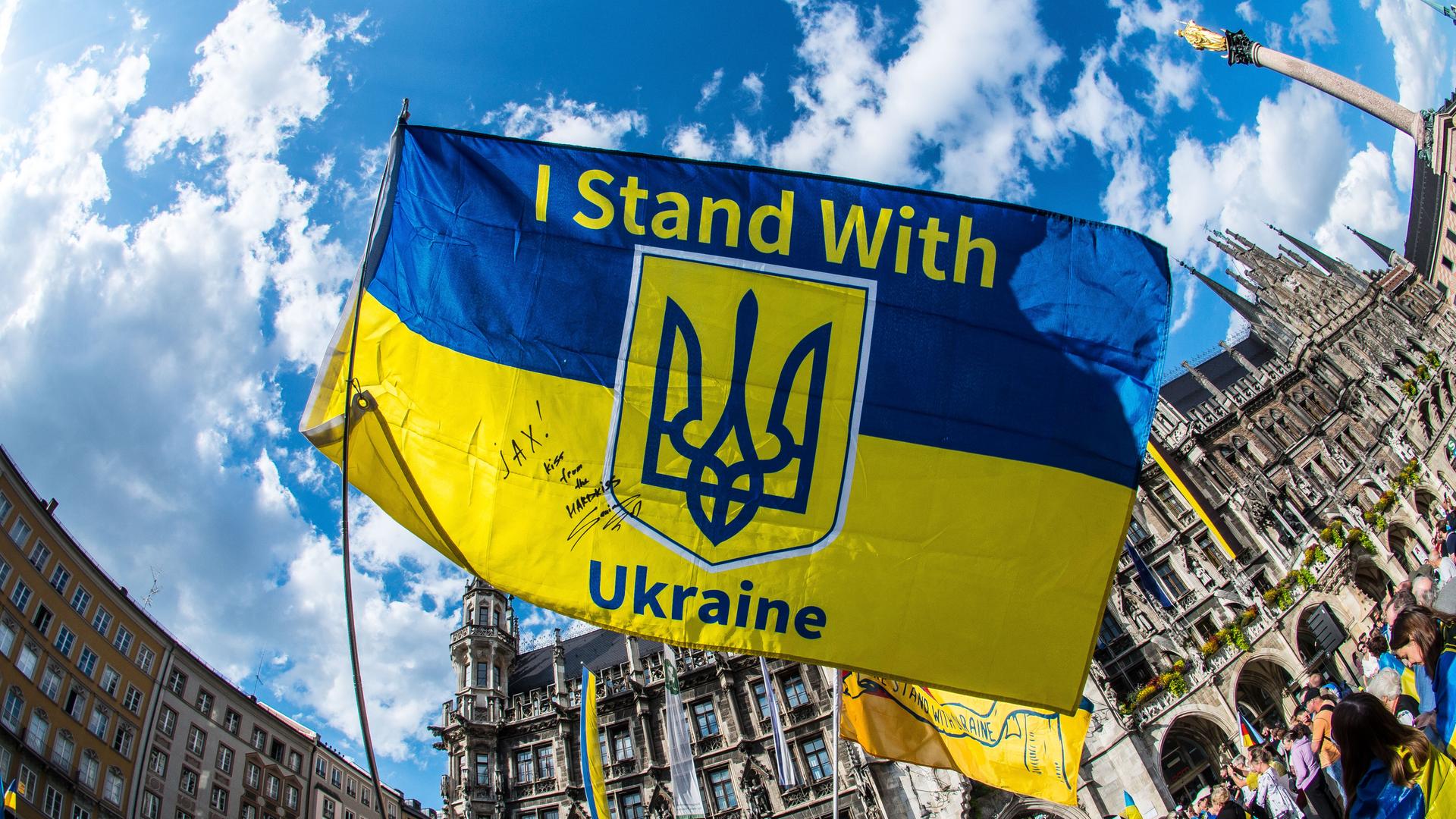 Bei einer Demonstration halten Protestierende ein Ukraine-Banner mit der Aufschrift "I stand with Ukraine" in die Höhe. 