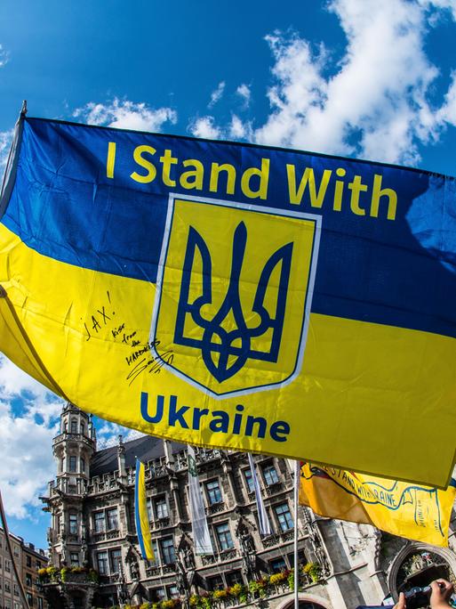 Bei einer Demonstration halten Protestierende ein Ukraine-Banner mit der Aufschrift "I stand with Ukraine" in die Höhe. 