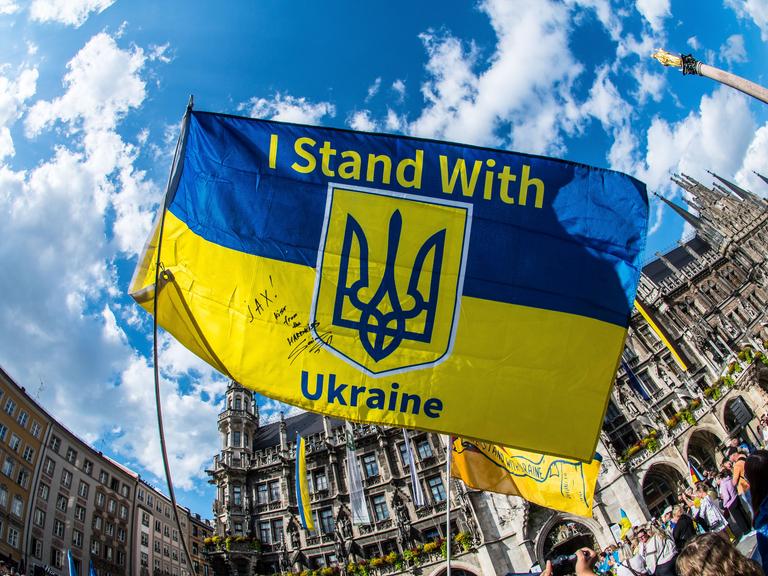 Bei einer Demonstration halten Protestierende ein Ukraine-Banner mit der Aufschrift "I stand with Ukraine" in die Höhe. 