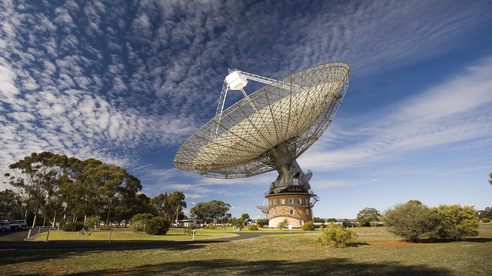Panorama-Blick auf ein Radioteleskop, das beeindruckend groß in einer Wiesenlandschaft steht.