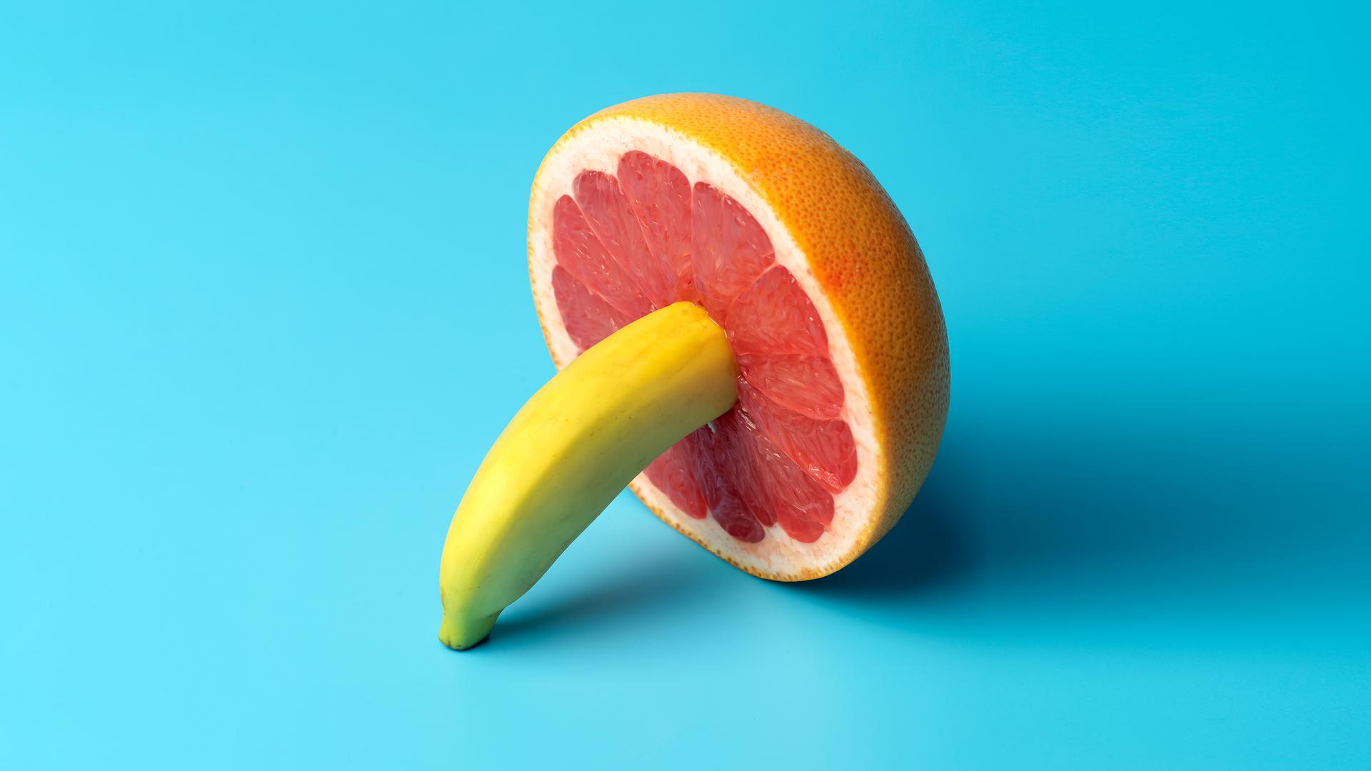 Minimalistische Darstellung einer Banane die in einer Grapefruit steckt auf blauem Grund. Minimalistische Darstellung einer Banane die in einer Grapefruit steckt auf blauem Grund.