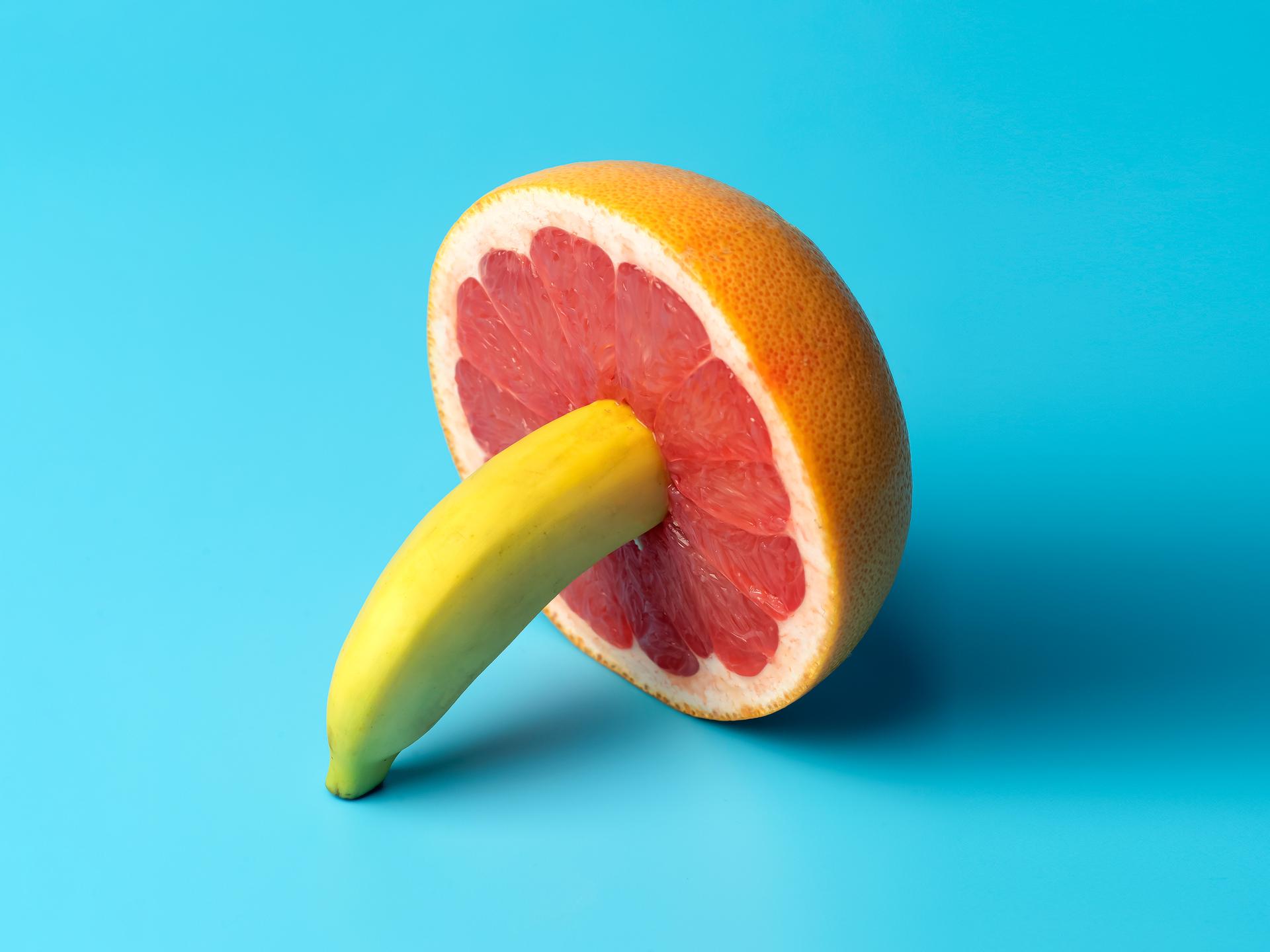 Minimalistische Darstellung einer Banane die in einer Grapefruit steckt auf blauem Grund.