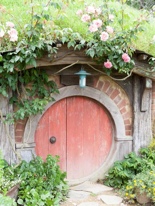 Ein winziges märchenhaftes Häuschen mit runder roter Holztür und einem kleinen Garten