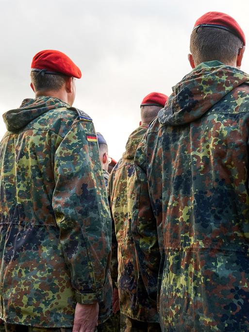 Soldaten der Bundeswehr stehen in Reih und Glied, gekleidet in Flecktarnuniformen und tragen rote sowie blaue Baretts