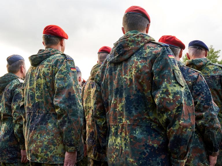 Soldaten der Bundeswehr stehen in Reih und Glied, gekleidet in Flecktarnuniformen und tragen rote sowie blaue Baretts