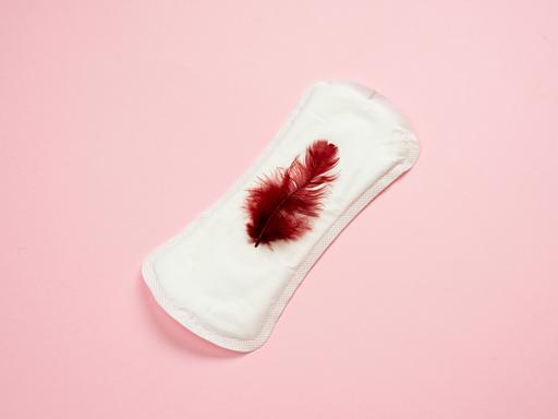 Eine weisse Menstruationsbinde mit einer roten Feder.