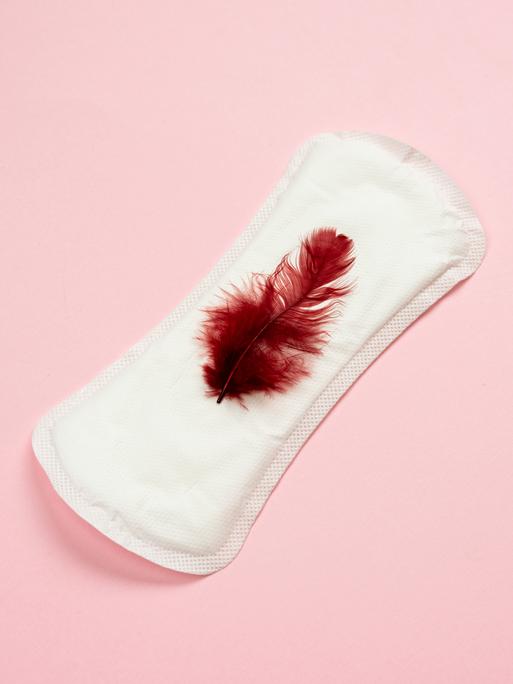 Eine weisse Menstruationsbinde mit einer roten Feder.